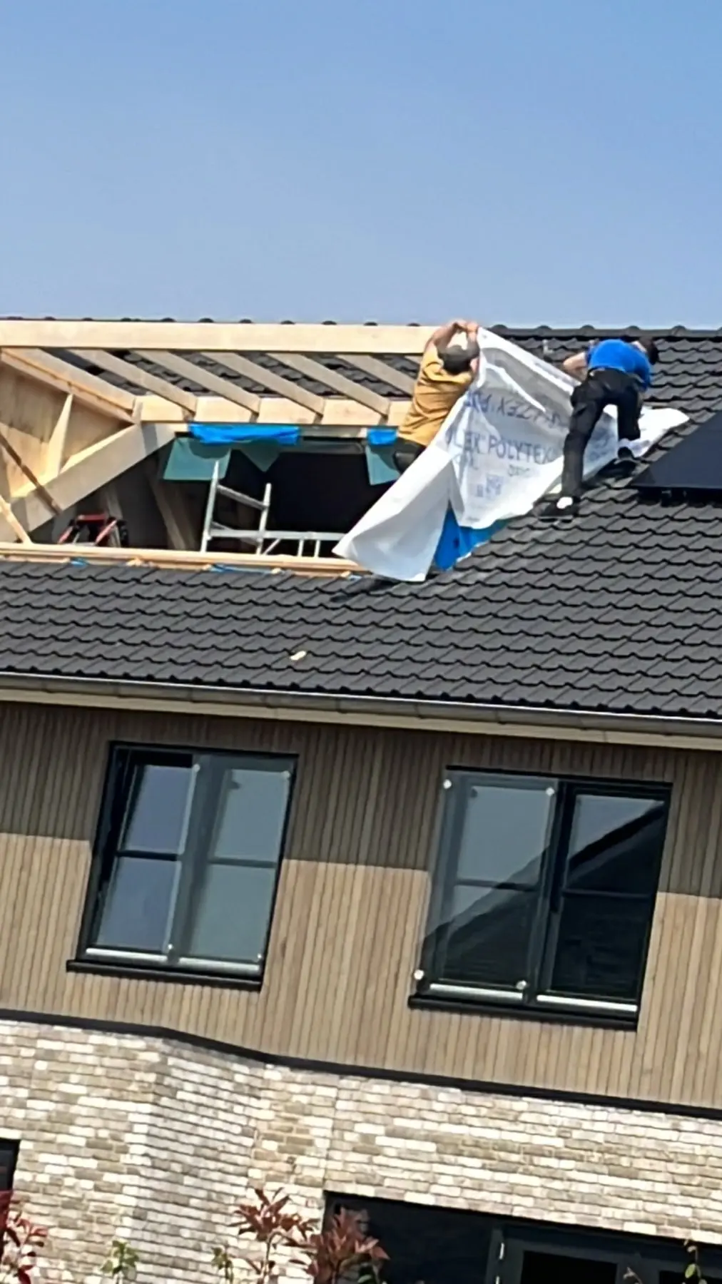 Twee dakdekkers brengen folie aan op een pannendak van een nieuwbouwwoning