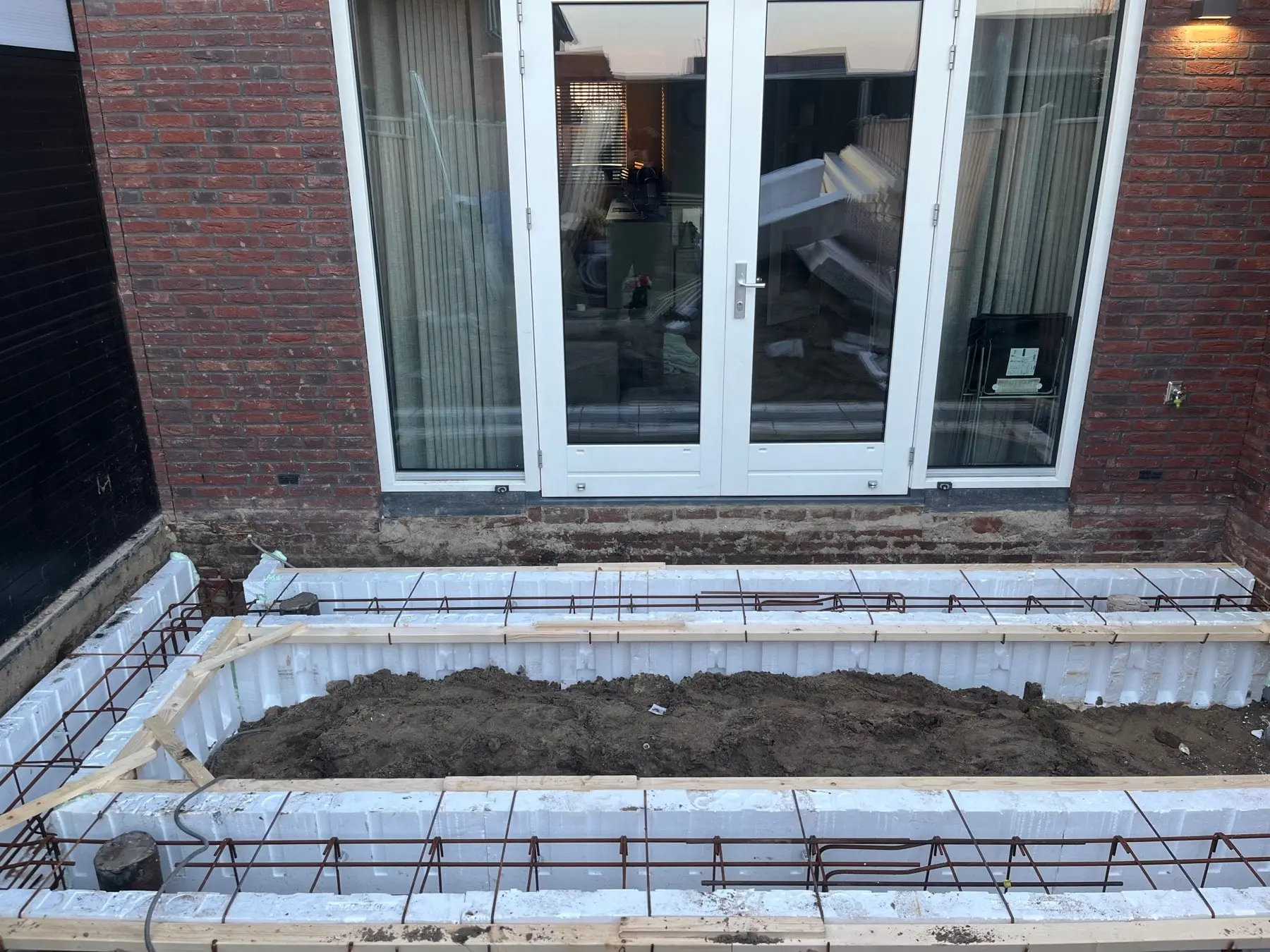 Bekisting met wapeningsstaal voor een nieuwe fundering achter een woning