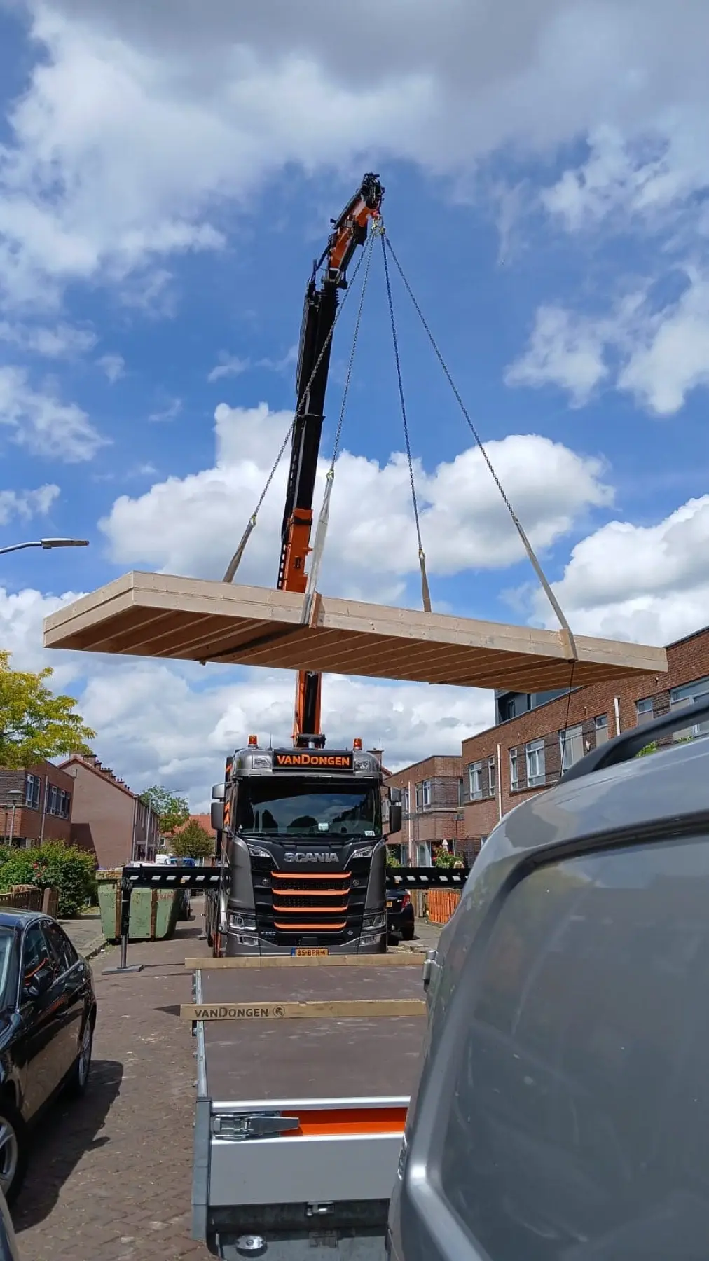 Kraan hijst een prefab vloerelement over de straat naar de achterzijde van een woning
