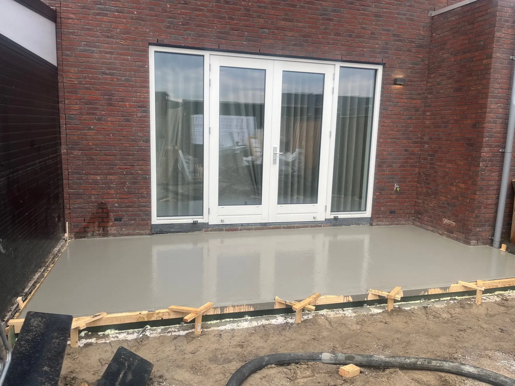 Afgewerkte betonvloer met bekisting rondom, achter een woning